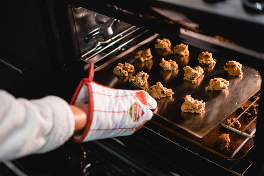 hand with oven mitt opening oven taking out cookie tray